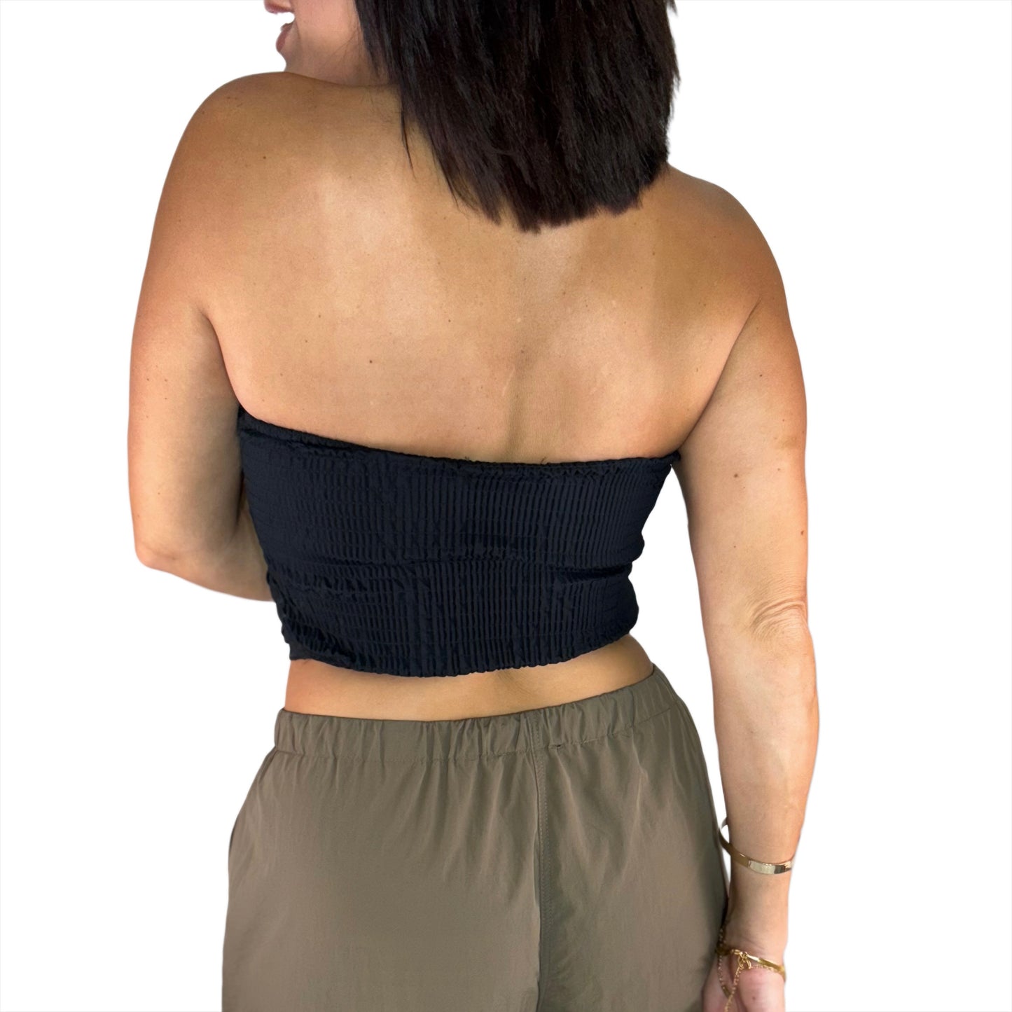 Woman modeling the back of a black strapless top and brown pants on a white background