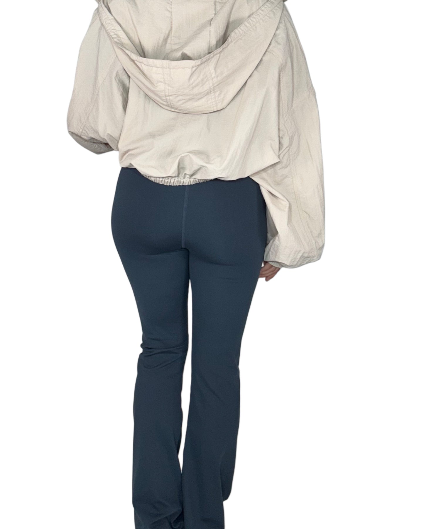 Woman wearing dark navy boot cut leggings and a tan jacket on a white background