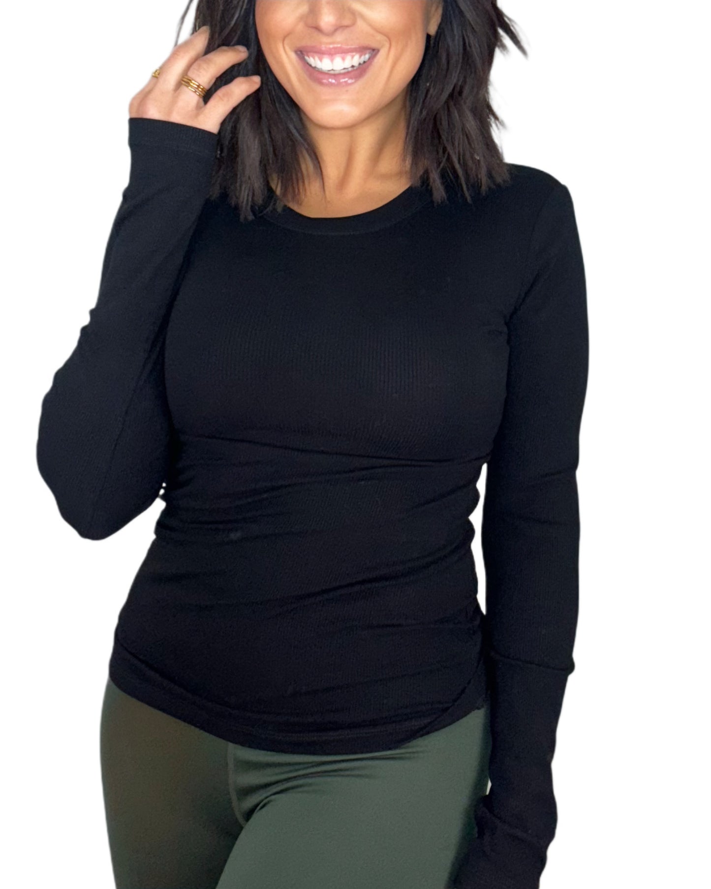 Woman wearing a black ribbed long-sleeve top and green active pants on a white background
