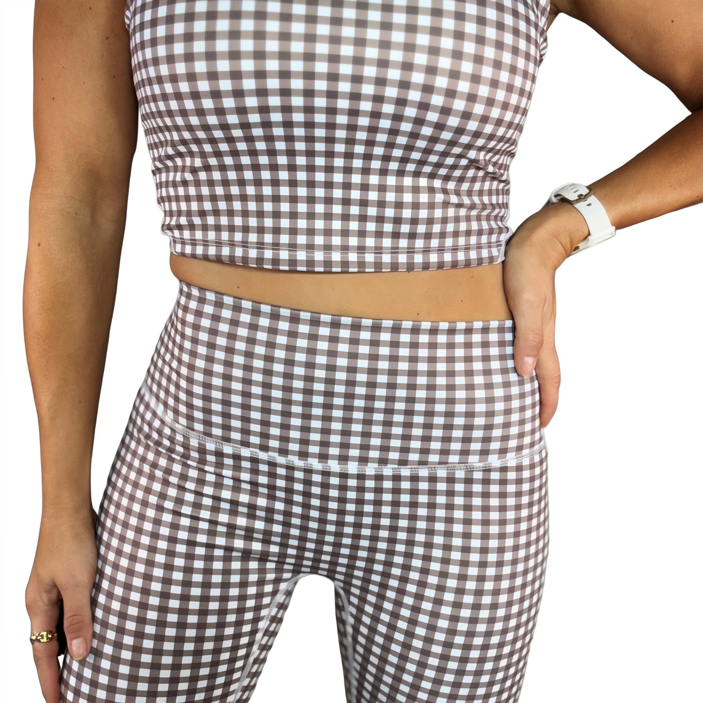 Close up of a woman wearing a brown and white gingham athletic set on a white background