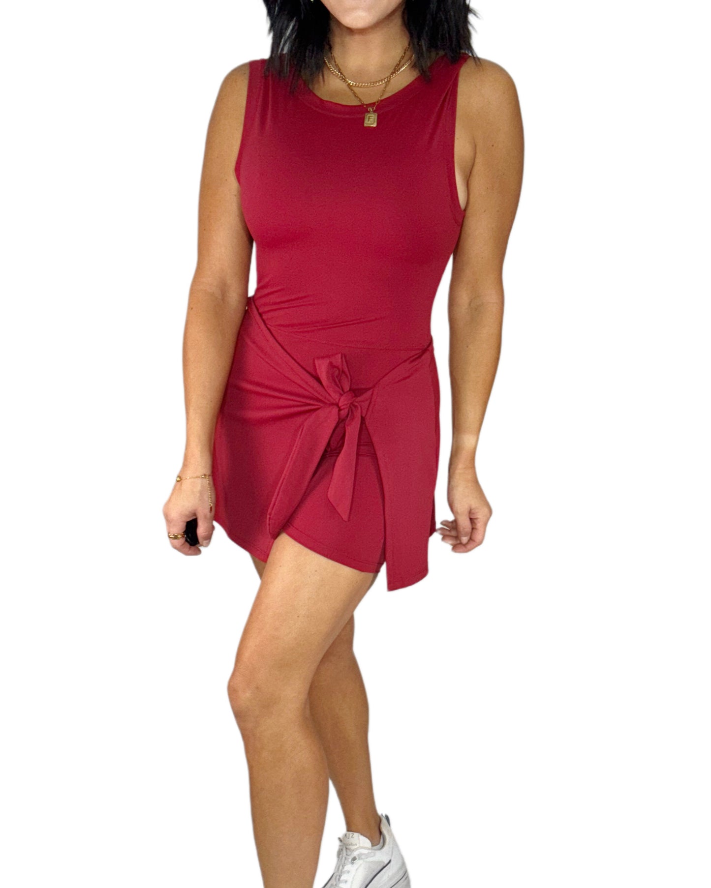 Side profile of a woman wearing a red active dress romper with a tie waist on white background