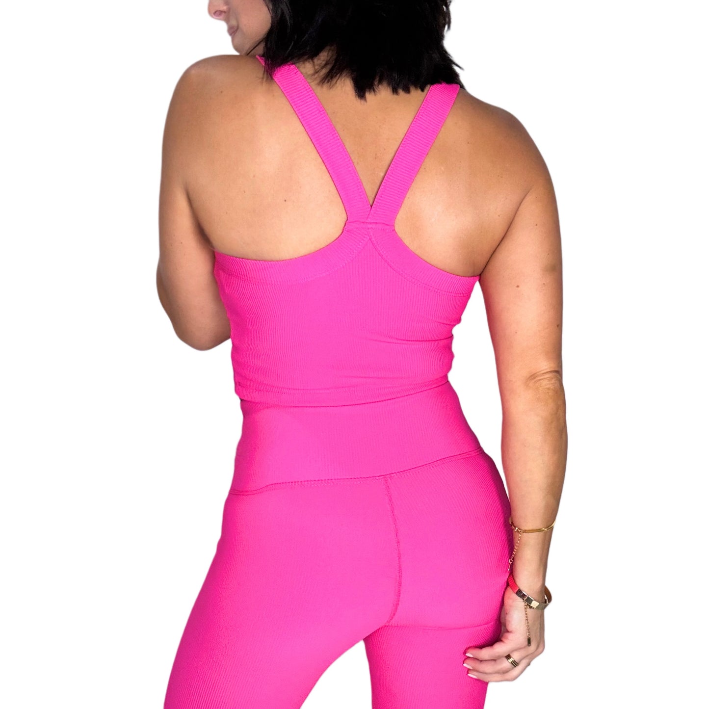 Back side of a woman wearing a bright pink ribbed athletic sports top with a white background