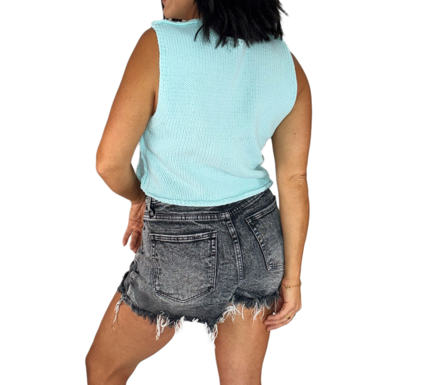 Back profile of a woman wearing a light blue sleeveless top and black denim shorts on a white background