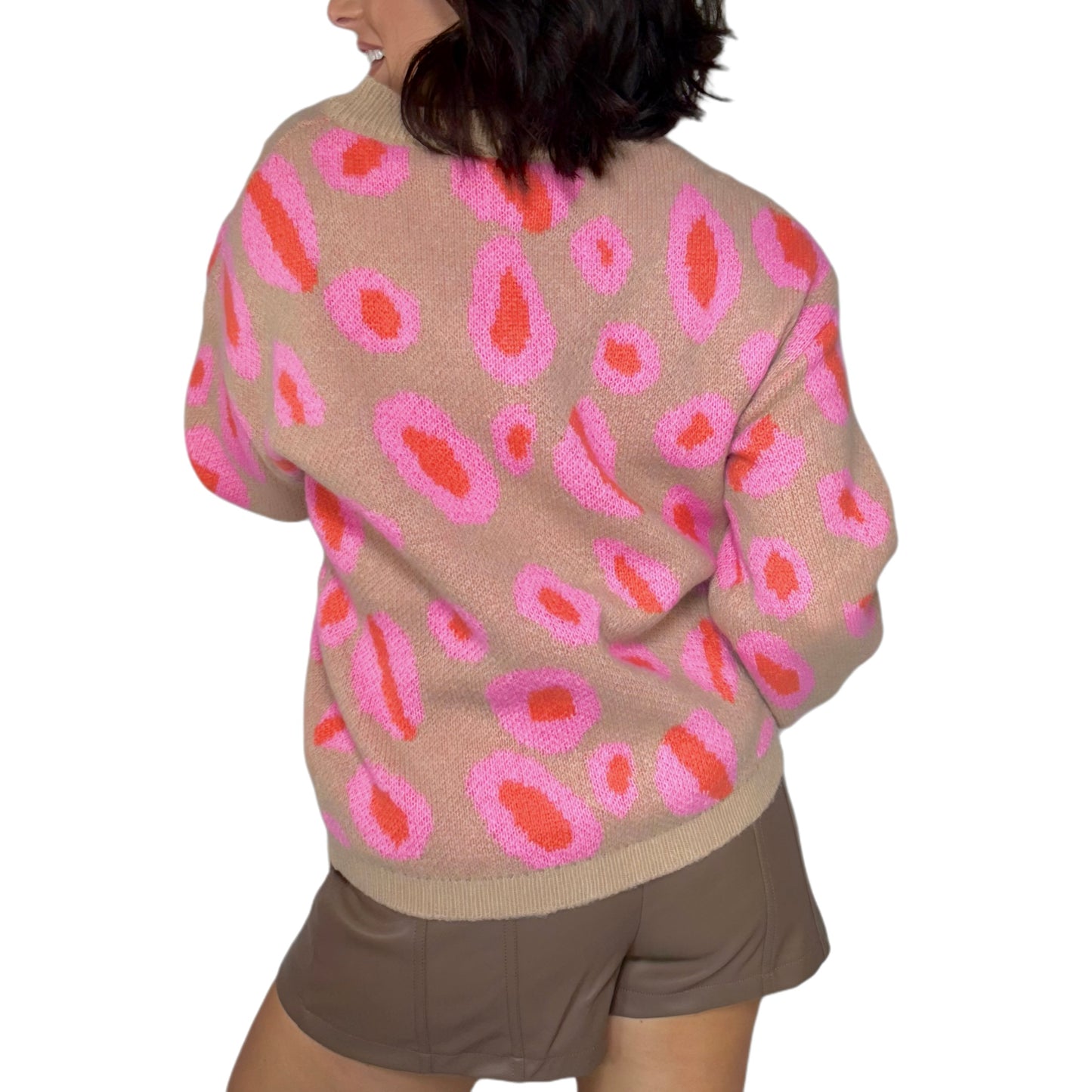 Woman turned around wearing a taupe sweater with pink and red leopard pattern on a white background