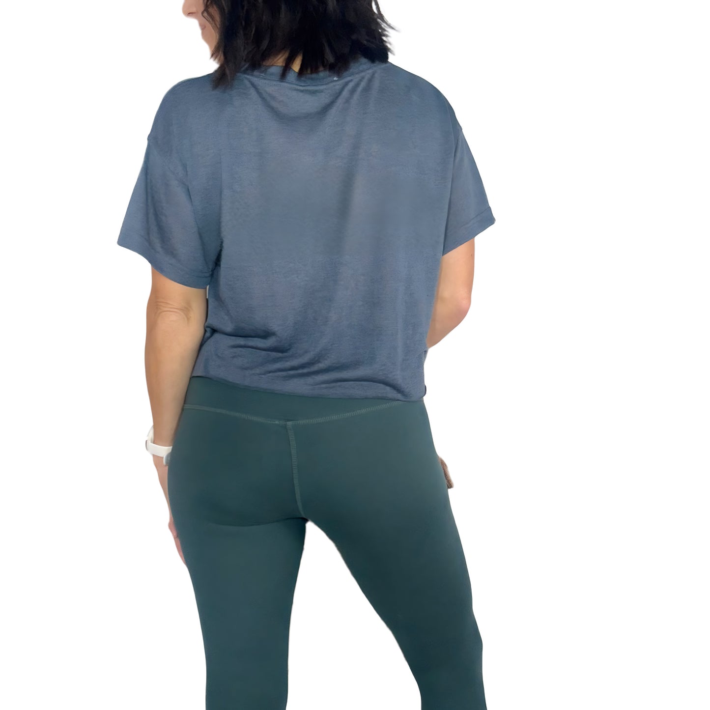 Woman turned around wearing a ash grey cropped tee and green active pants on a white background