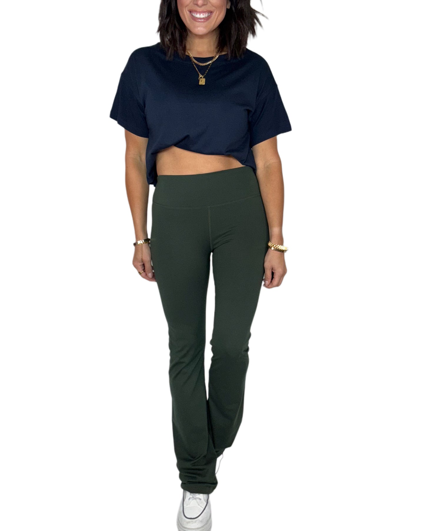 Woman wearing a navy top and forest green bootcut leggings on a white background