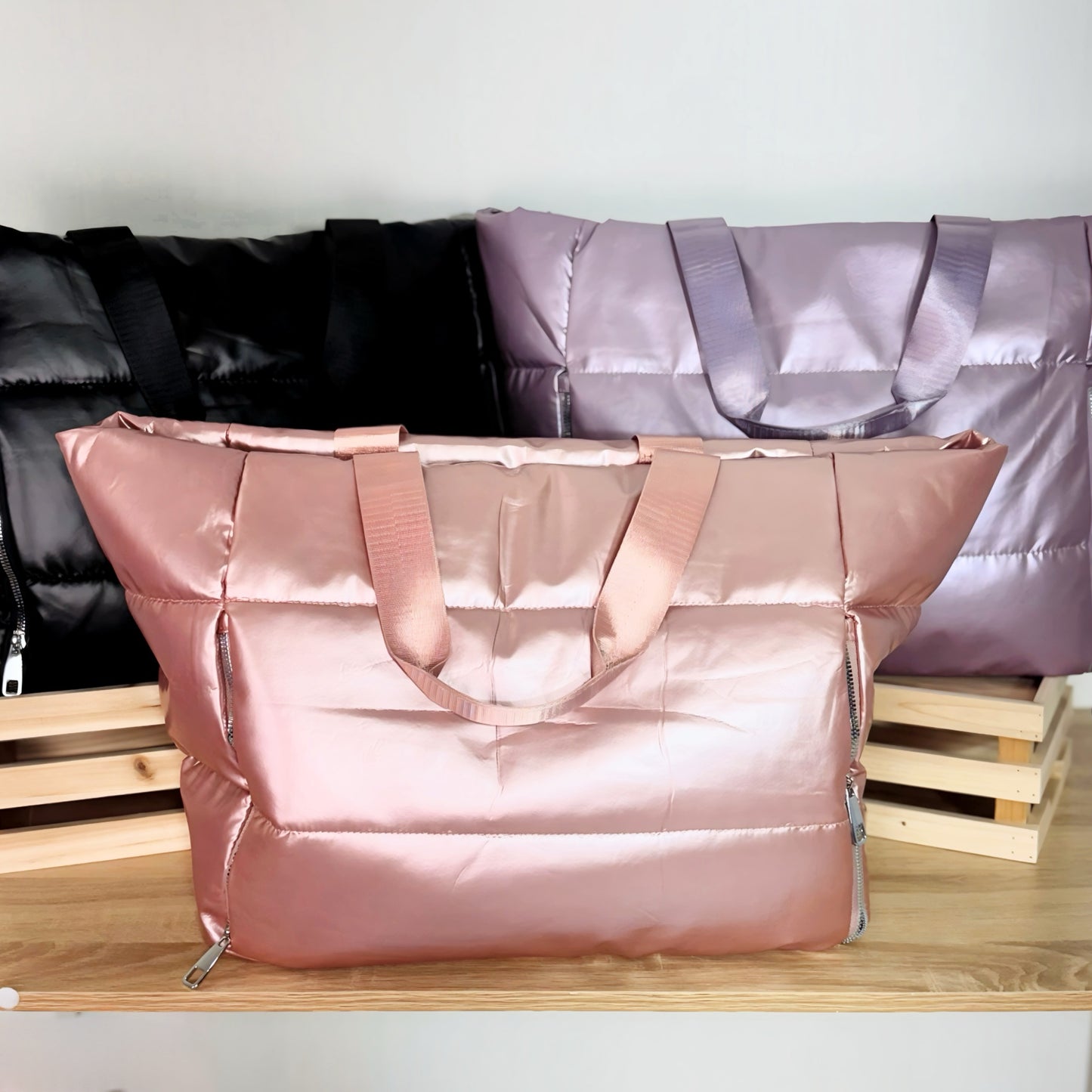 Large puffer tote bags in pink, black and lavender on a white background and light wood table