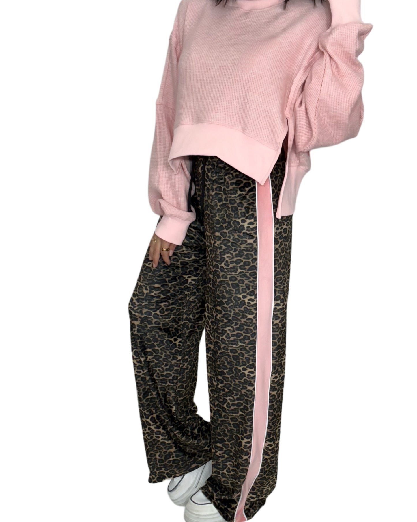 Side view of a woman wearing a pink oversized top and leopard print pants with a pink stripe on a white background