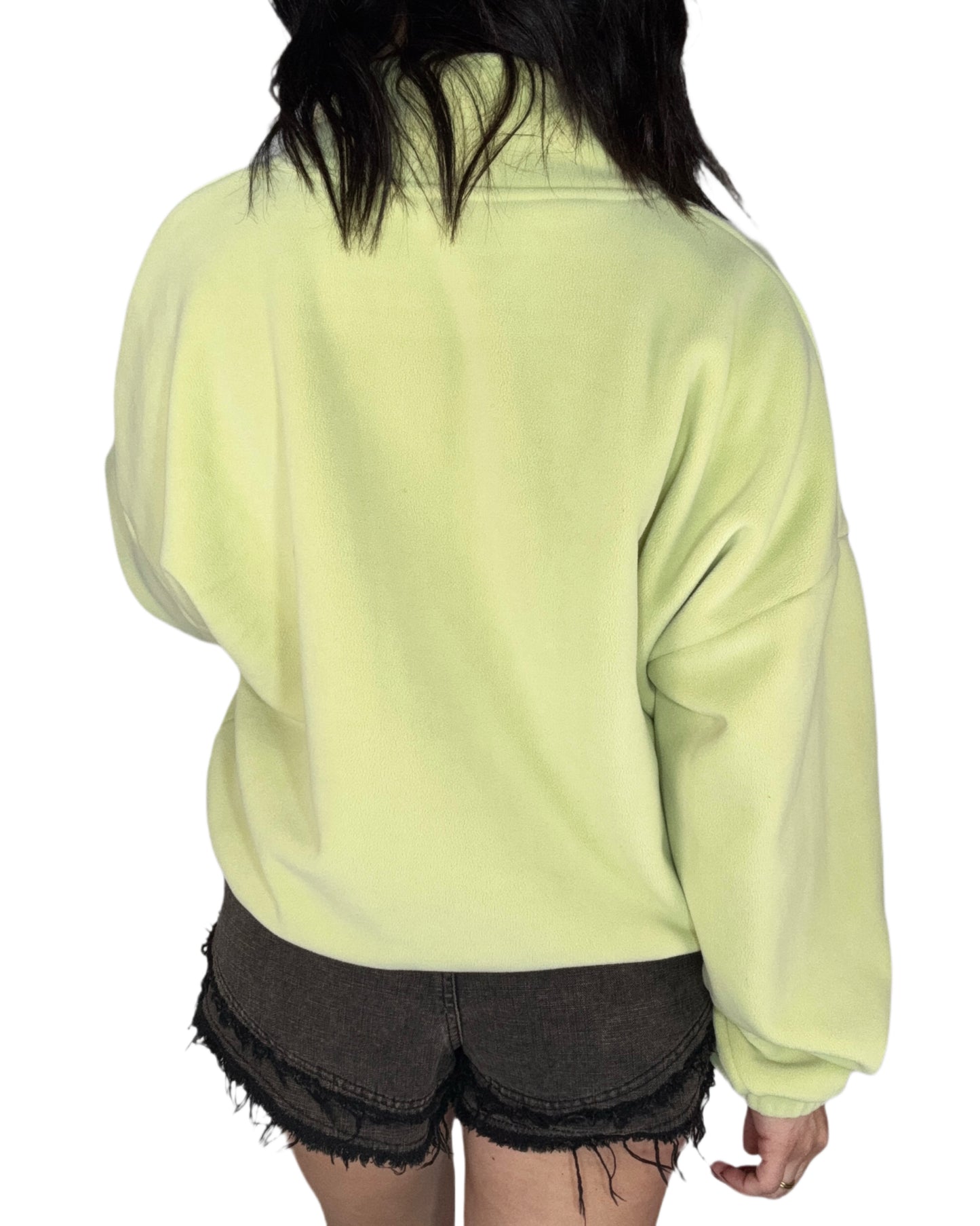 Back profile of a woman wearing a light green fleece jacket, in black shorts on a white background