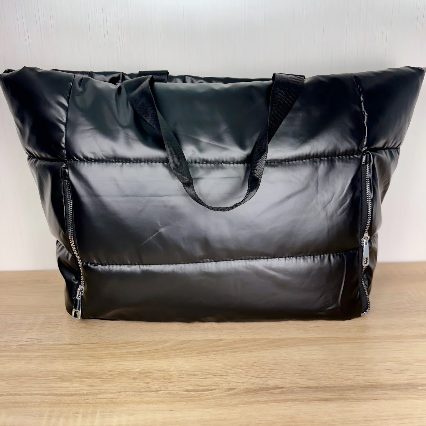 large black puffer travel tote on a light wood table and a white backdrop