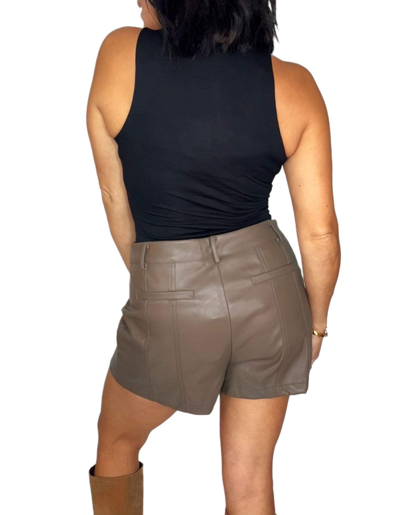 Back profile of a woman wearing a black sleeveless bodysuit and brown leather shorts on a white background