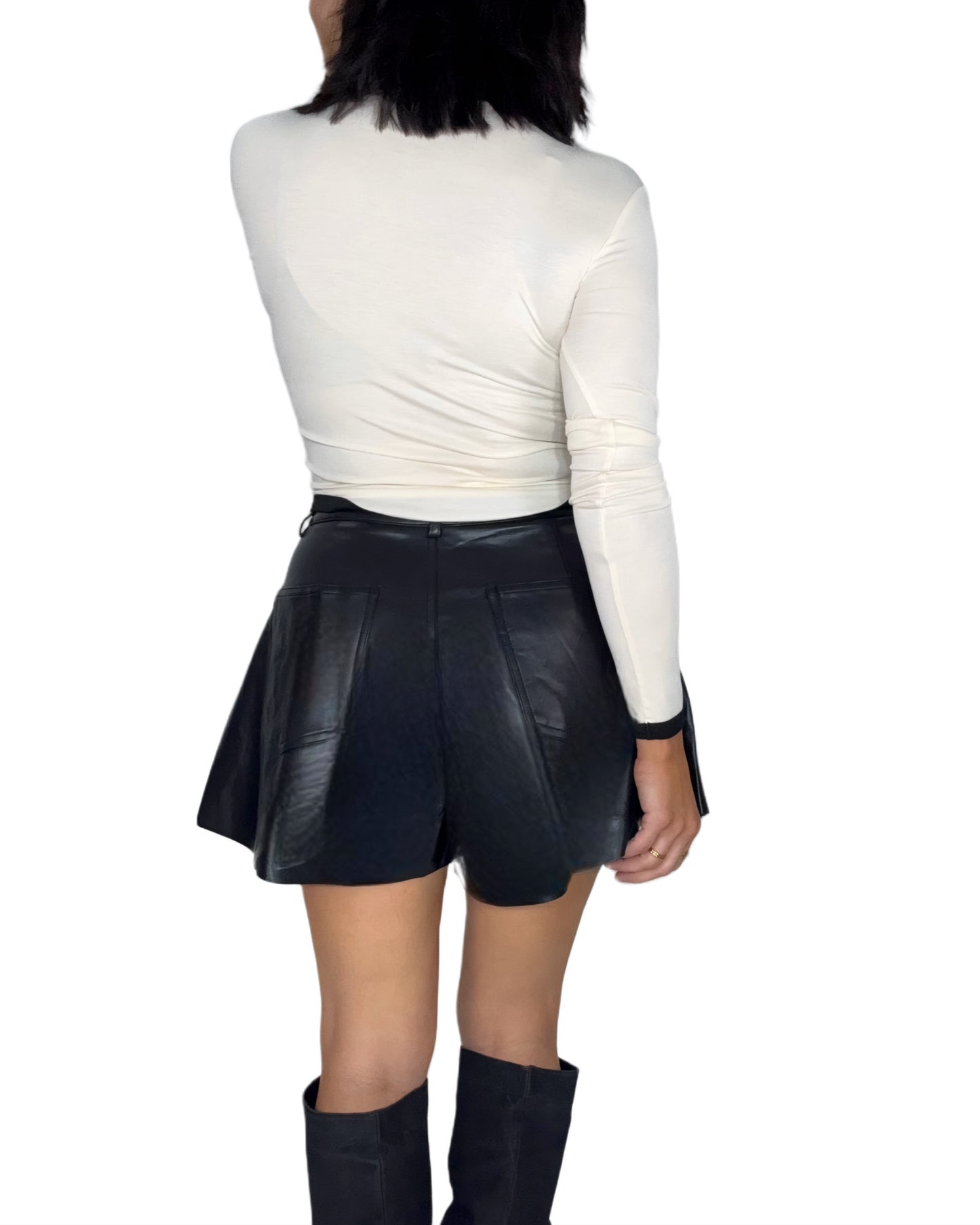 Back side of a woman wearing a white long-sleeve top and black leather shorts on a white background