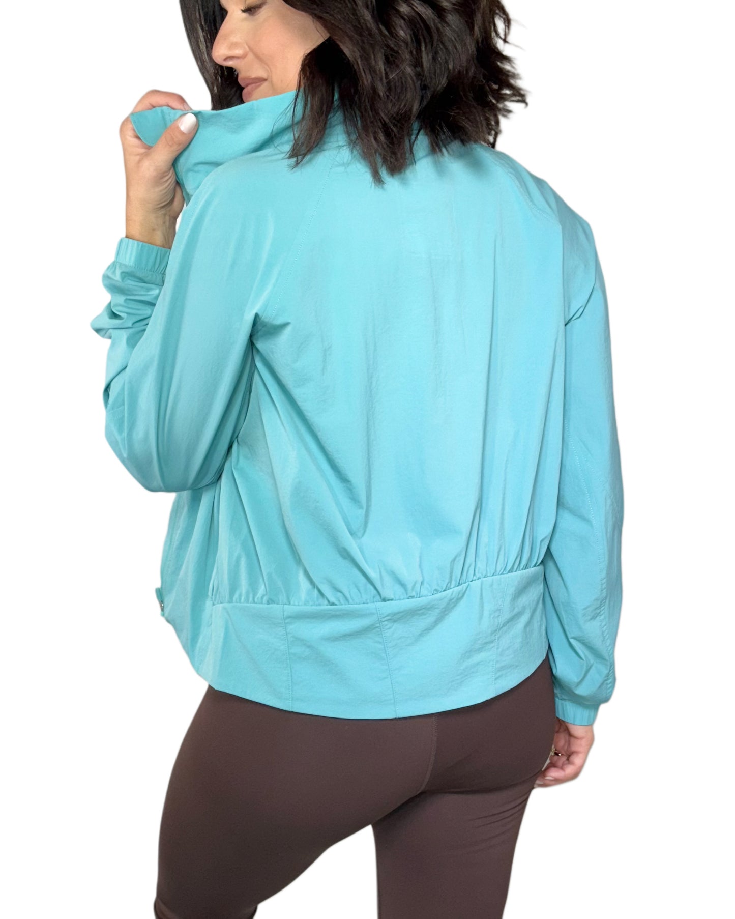 Woman turned around wearing a aqua athletic jacket on a white background