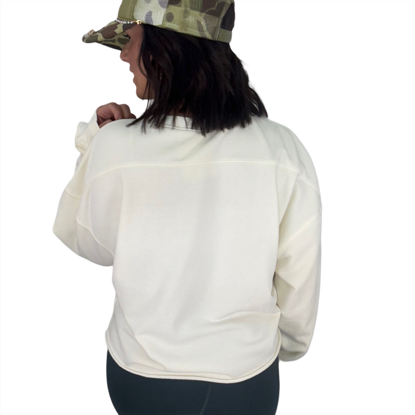 Woman turned around wearing a white sweatshirt and camouflage cap on a white background