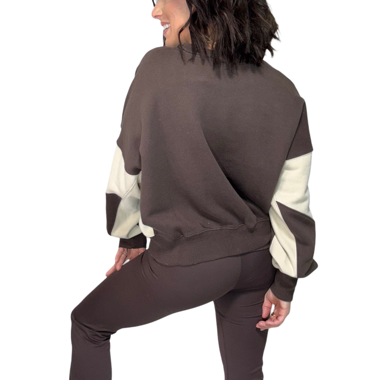The back of a woman wearing a brown and cream color-blocked outfit on a white background