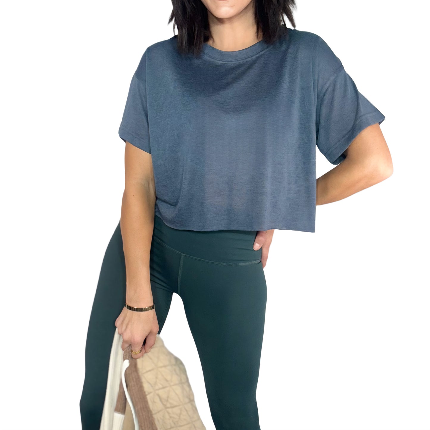 Woman wearing a ash grey cropped tee and green active pants with cream jacket on a white background