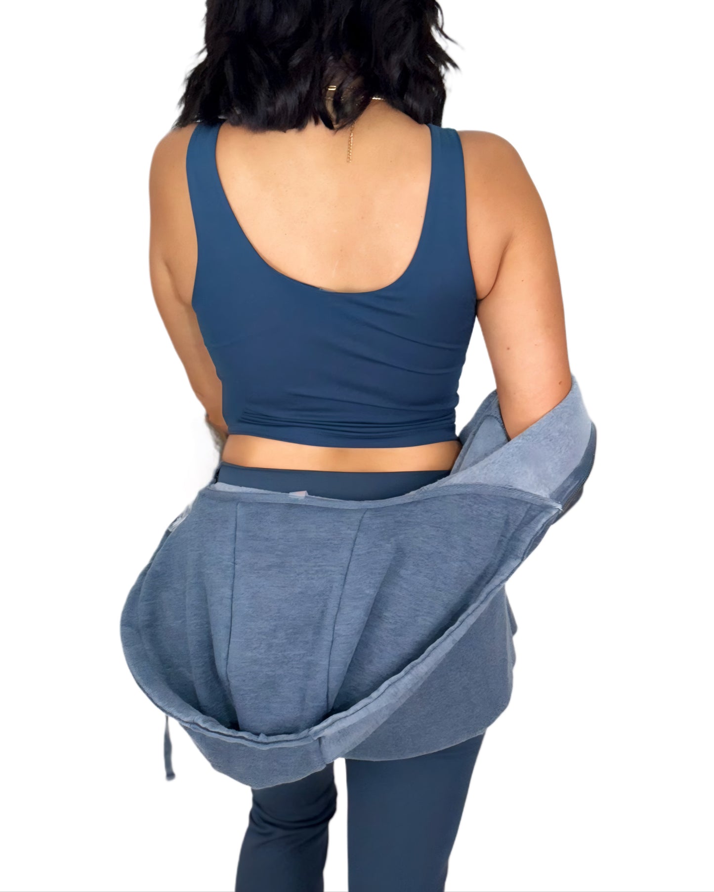 Woman turned around wearing a navy athletic set and a navy jacket on a white background