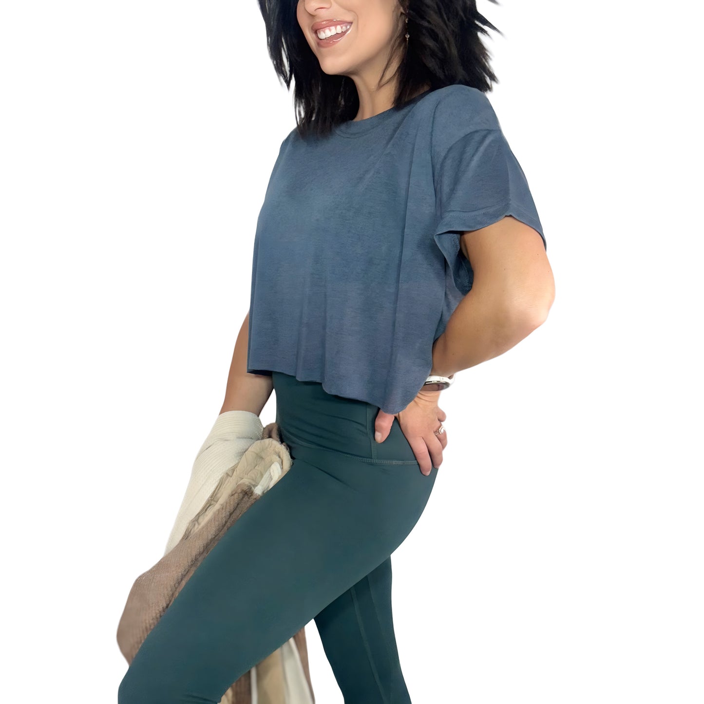 Side profile of a woman wearing a ash grey cropped tee and green active pants with cream jacket on a white background