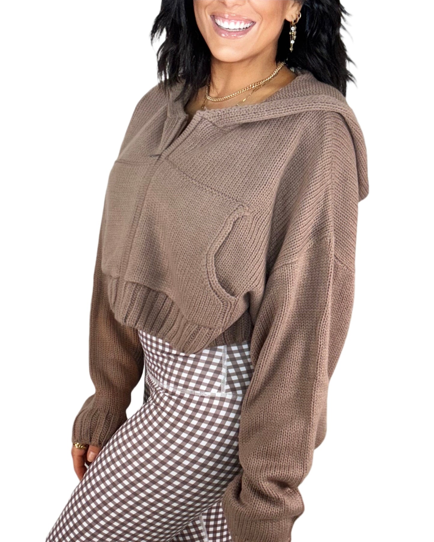 Side profile of a woman wearing a brown knit jacket and brown gingham bottoms on a. white background