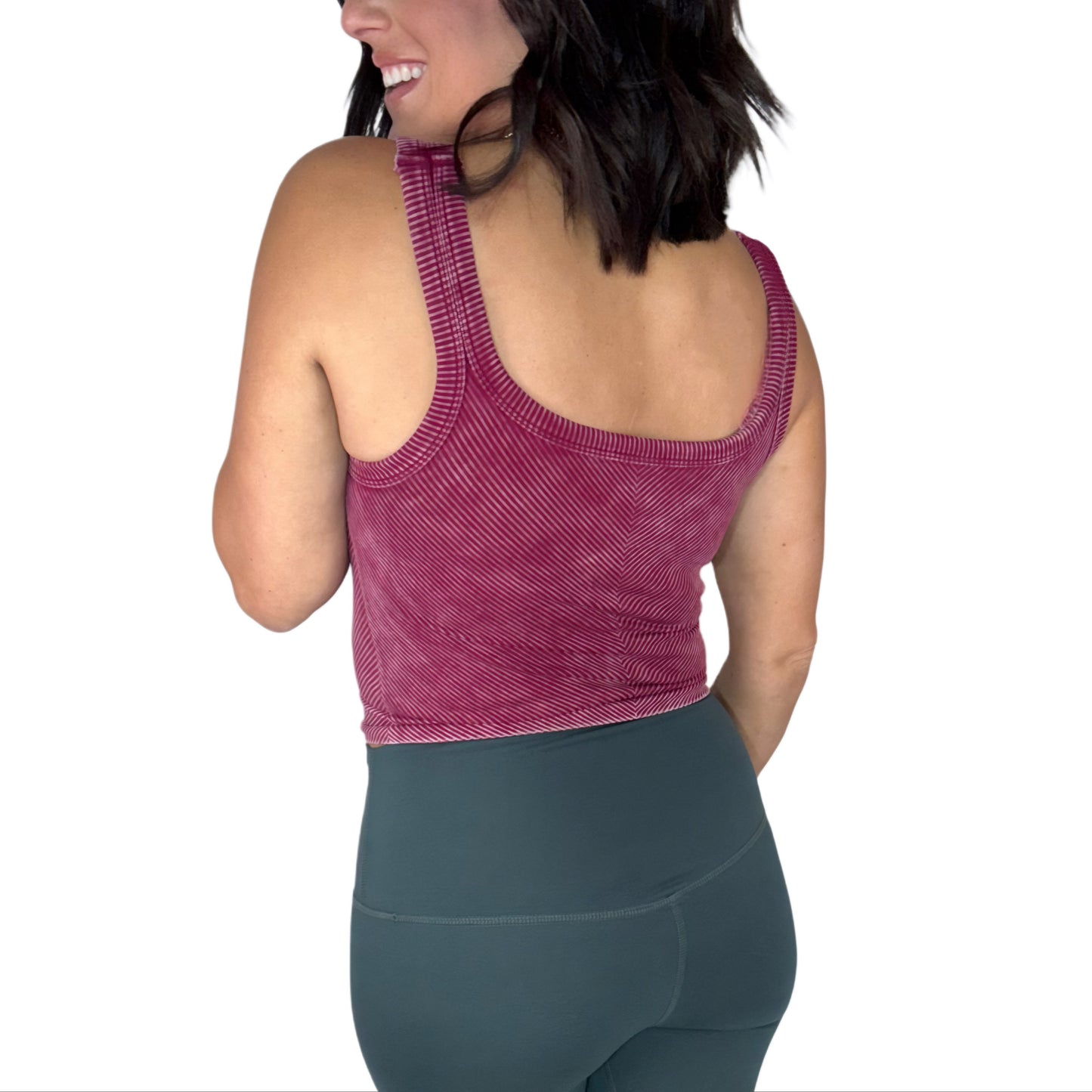 Back side of a woman wearing a maroon ribbed athletic top and green leggings on a white background