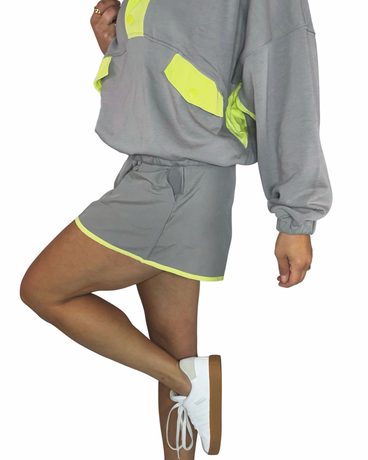 Side profile of a woman wearing a stone taupe short set with lime accents and white tennis shoes on a white background