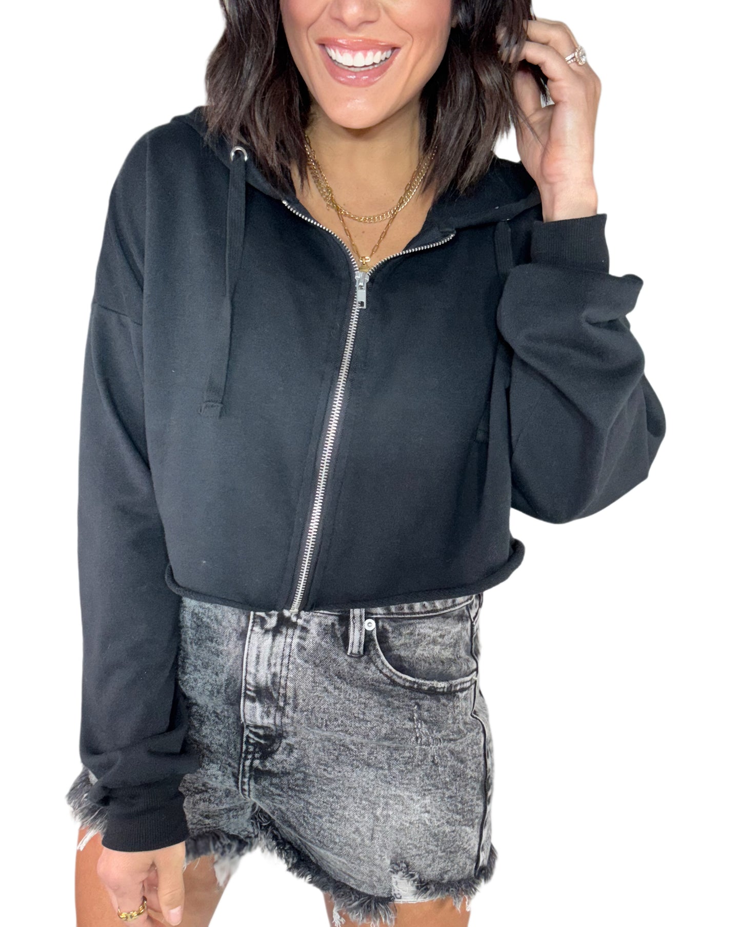 Woman wearing a black raw hemmed cropped zip up jacket with black denim shorts and a white background