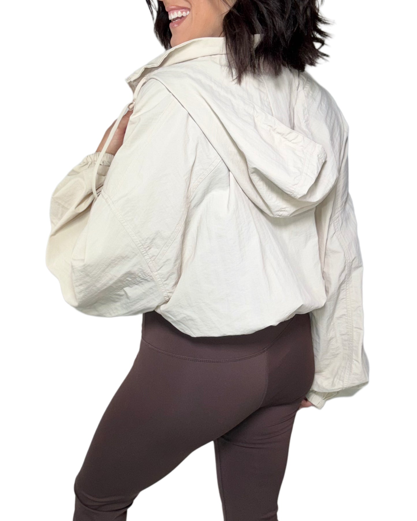 Woman wearing a tan windbreaker jacket and brown active pants with a white background