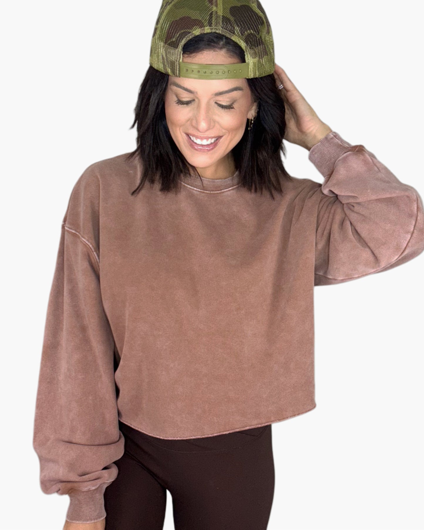 Woman wearing a mauve sweatshirt and green camo cap and brown leggings on a white background