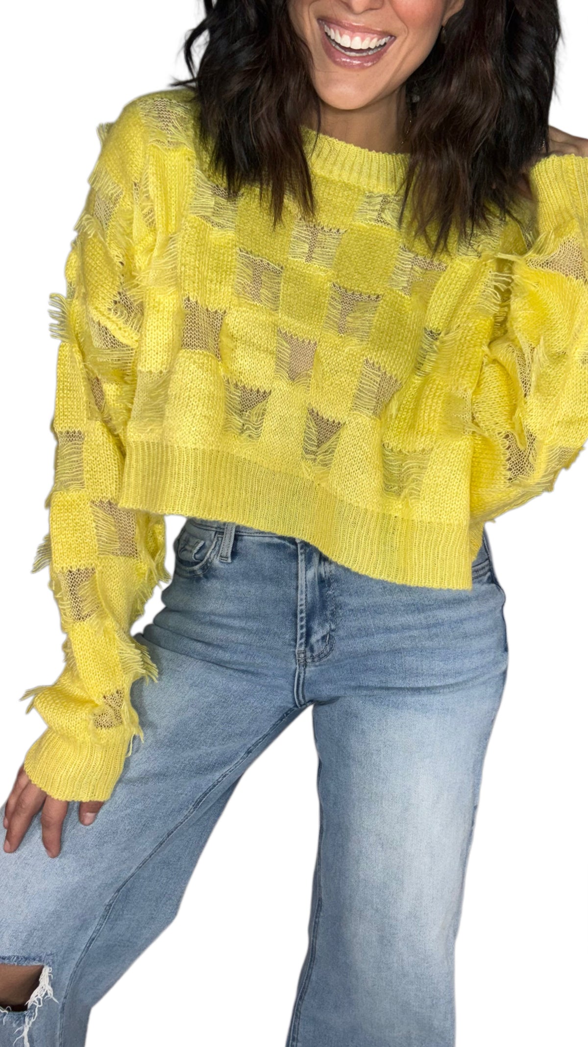 Close up of a woman wearing a yellow relaxed fit sweater top with distressed details, paired with medium washed jeans on a white background