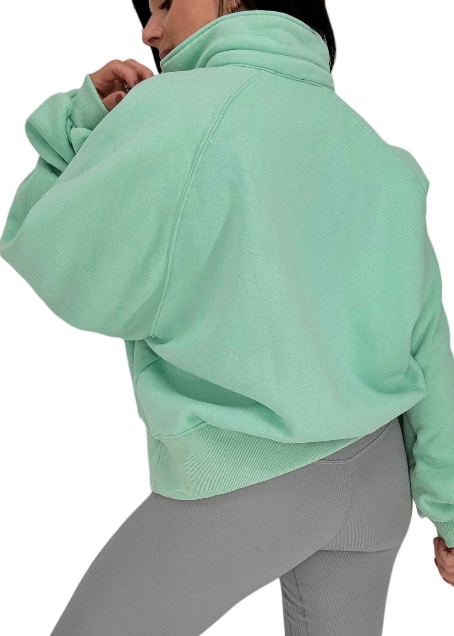 Back side of a woman wearing a light green sweatshirt and gray leggings on a white background