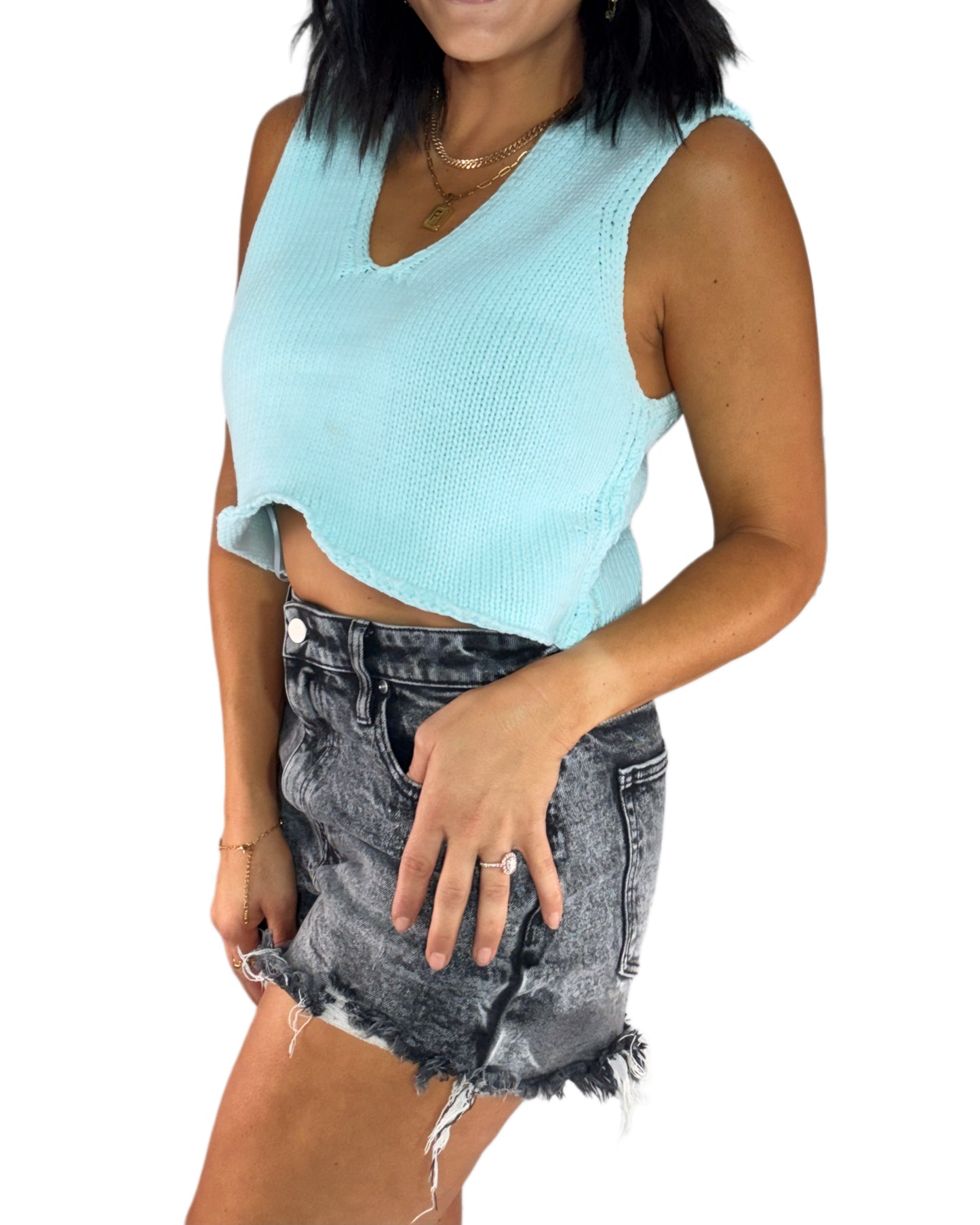 Side profile of a woman wearing a light blue sleeveless knit top and black denim shorts on a white background