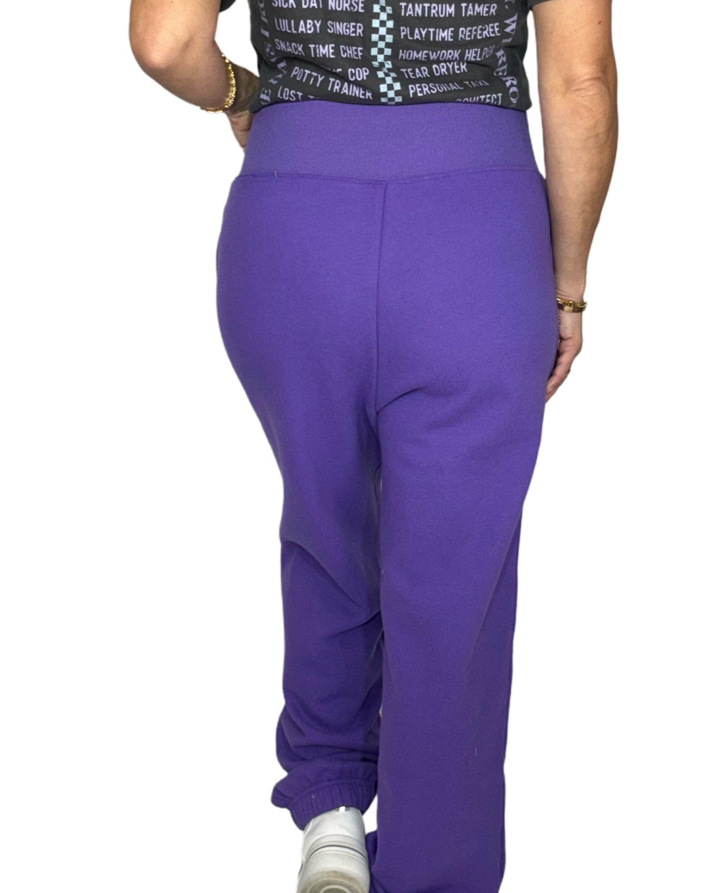 Woman turned around wearing purple joggers and graphic tee on a white background