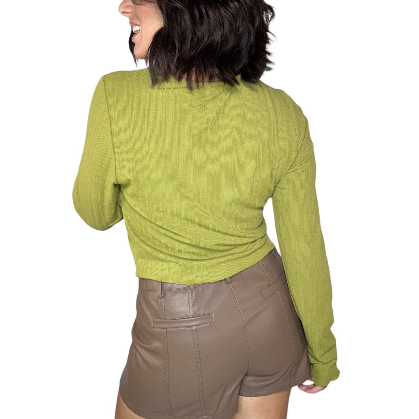 Woman turned around wearing a green tie-up top and brown shorts on a white background
