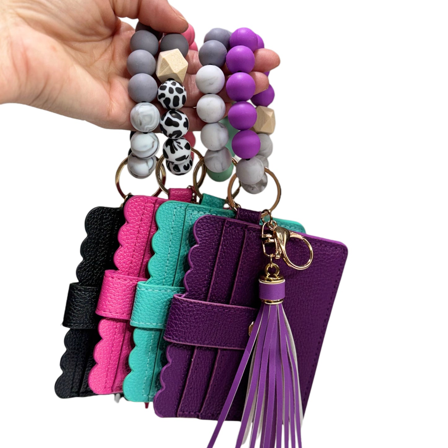 Colorful keychains with beads and leather accents held by a hand on a white background