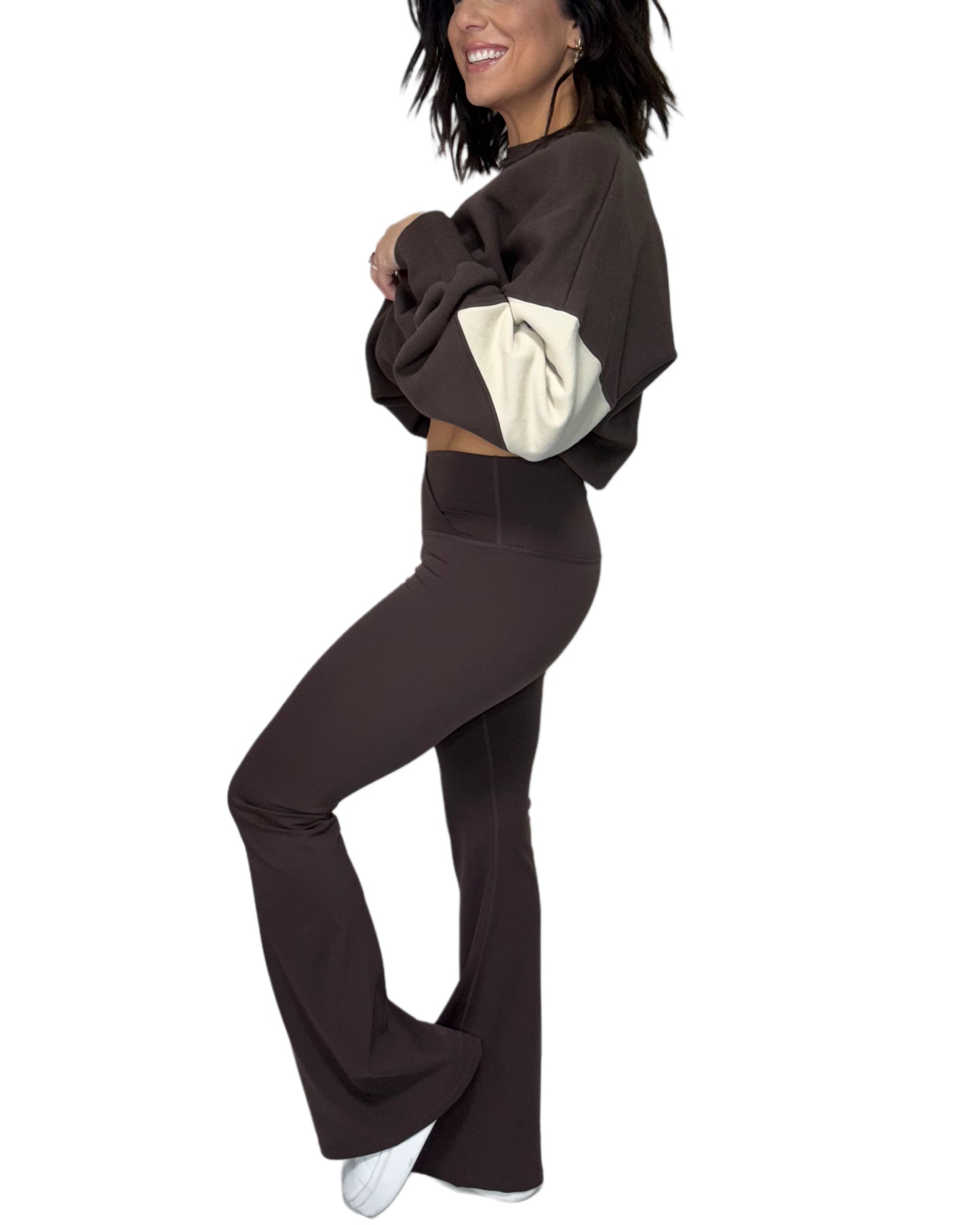 Side profile of woman wearing brown flared active pants with a brown and cream sweatshirt on a white background