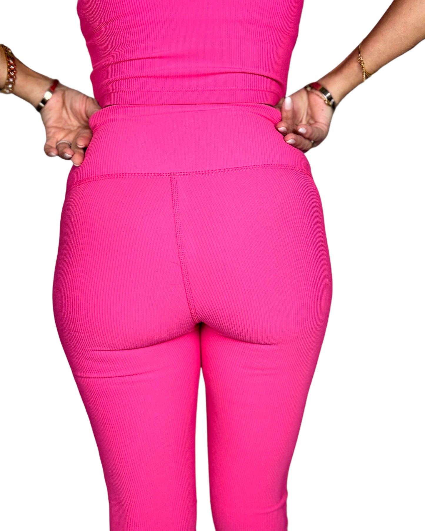 Back side of a woman wearing bright pink ribbed leggings on a white background