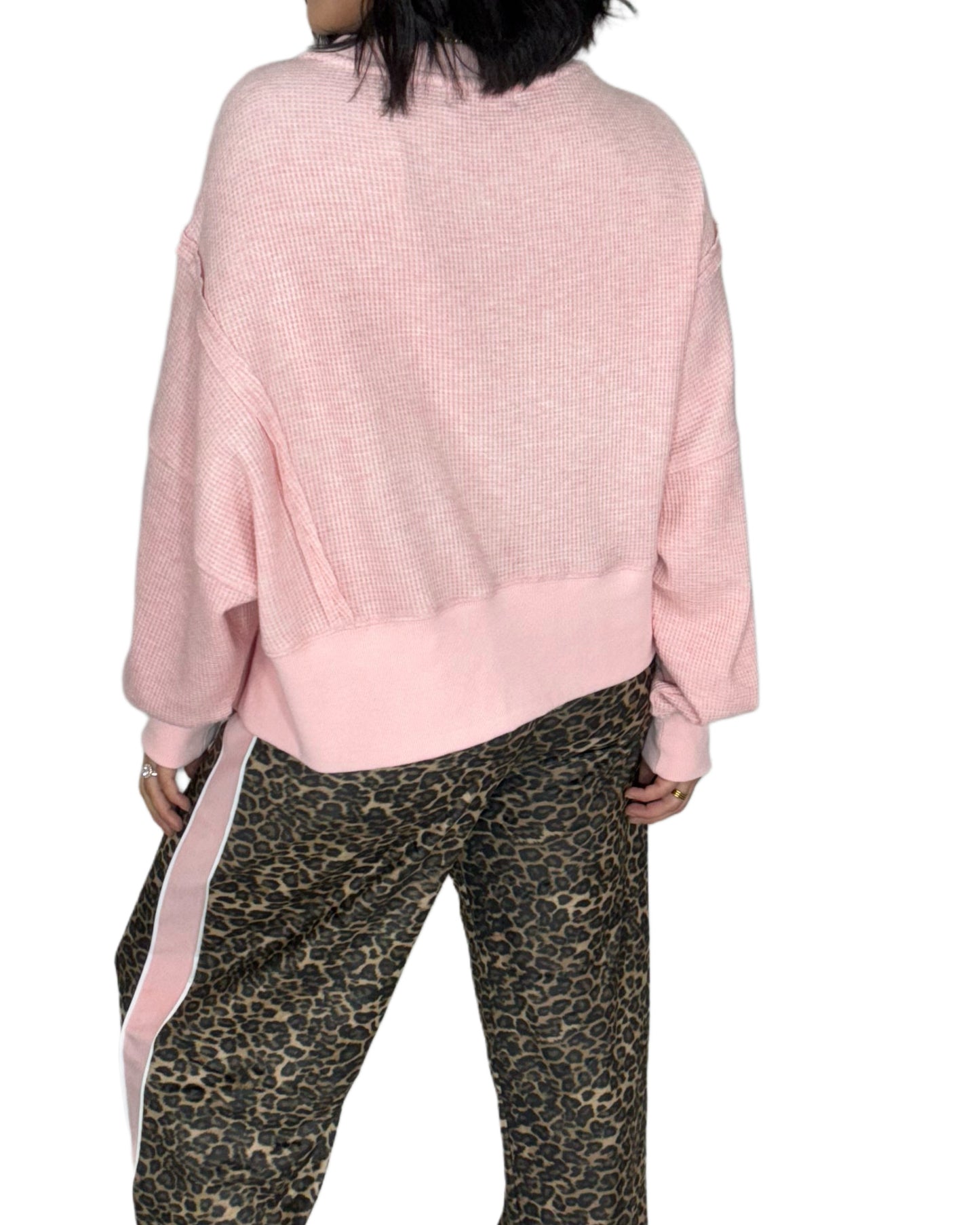 Back profile of a woman wearing a pink waffle sweatshrirt and leopard print pants on a white background