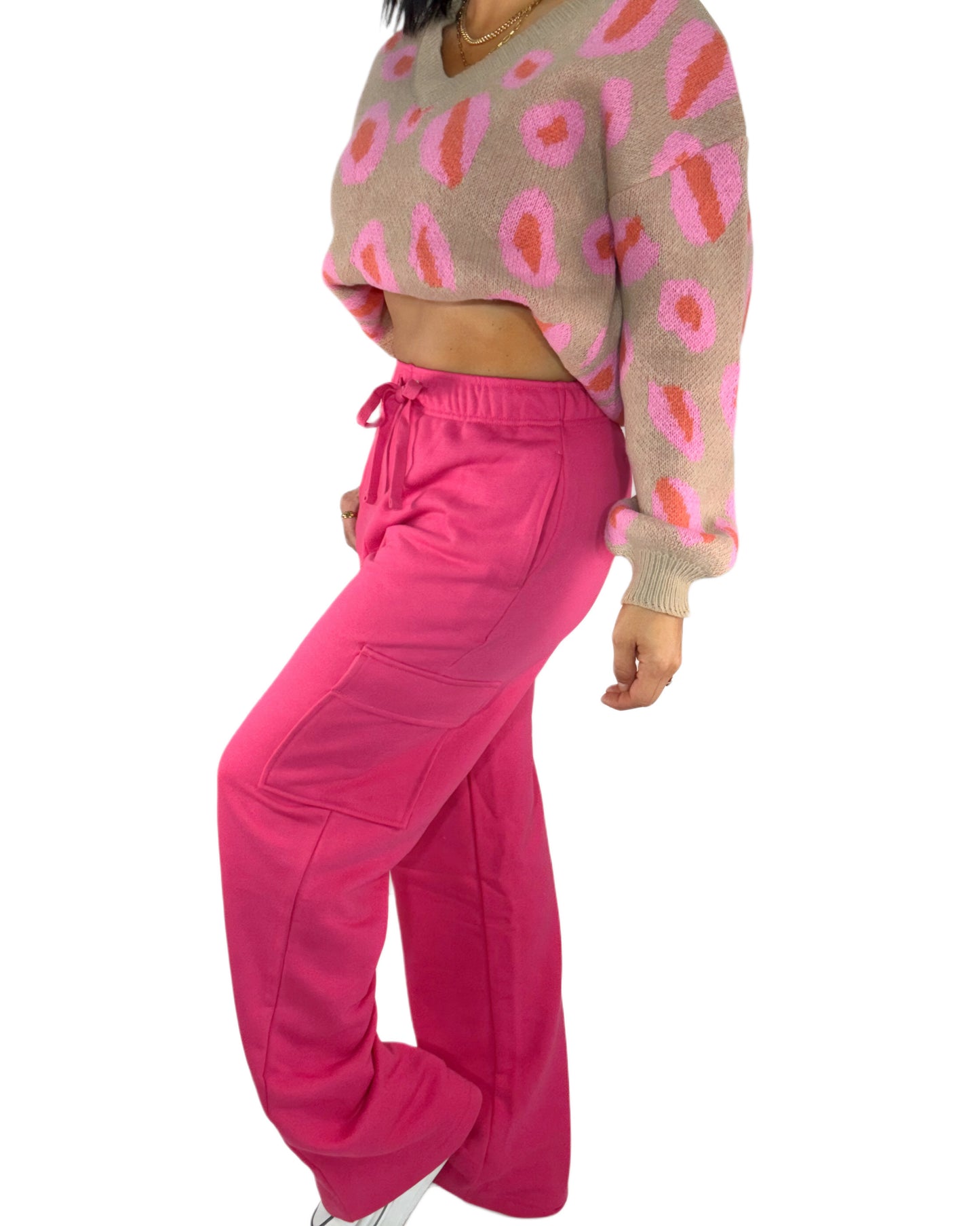 Side profile of a woman wearing a patterned sweater and bright pink pants on a white background