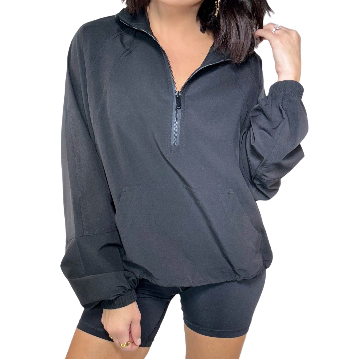 Woman wearing black quarter zip active jacket, black shorts and a white background