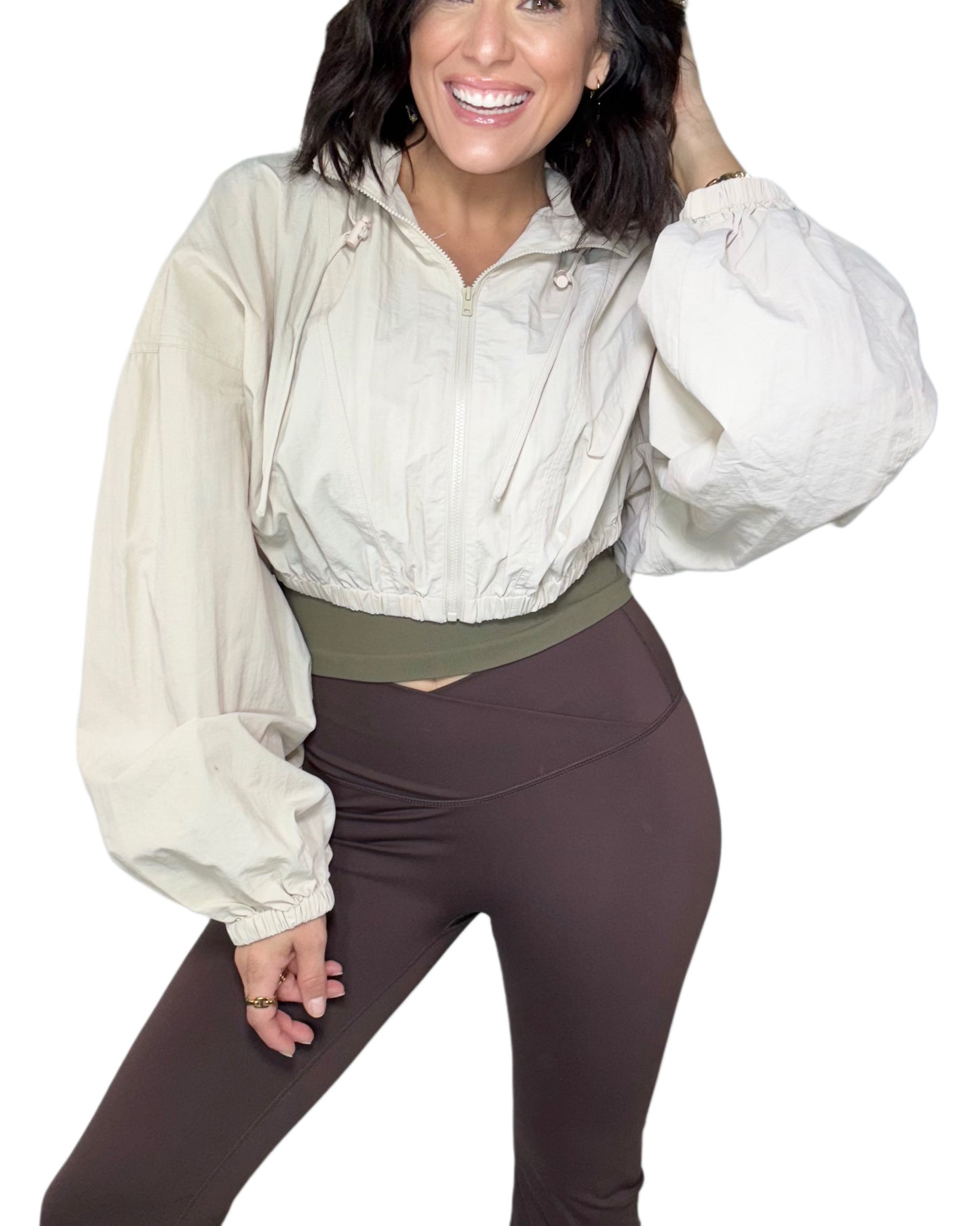 Woman wearing a tan long-sleeve wind breaker and brown active pants on a white background