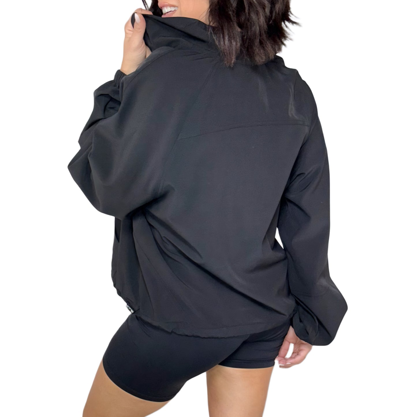 Woman turned around wearing a black quarter zip jacket and shorts on a white background