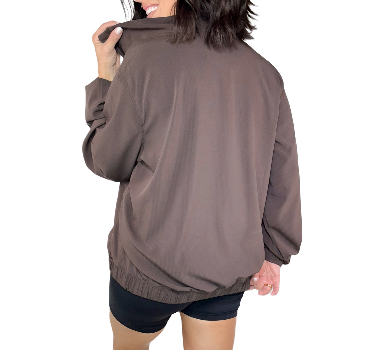 Woman wearing a brown ribbed zip up on a white background, turned around