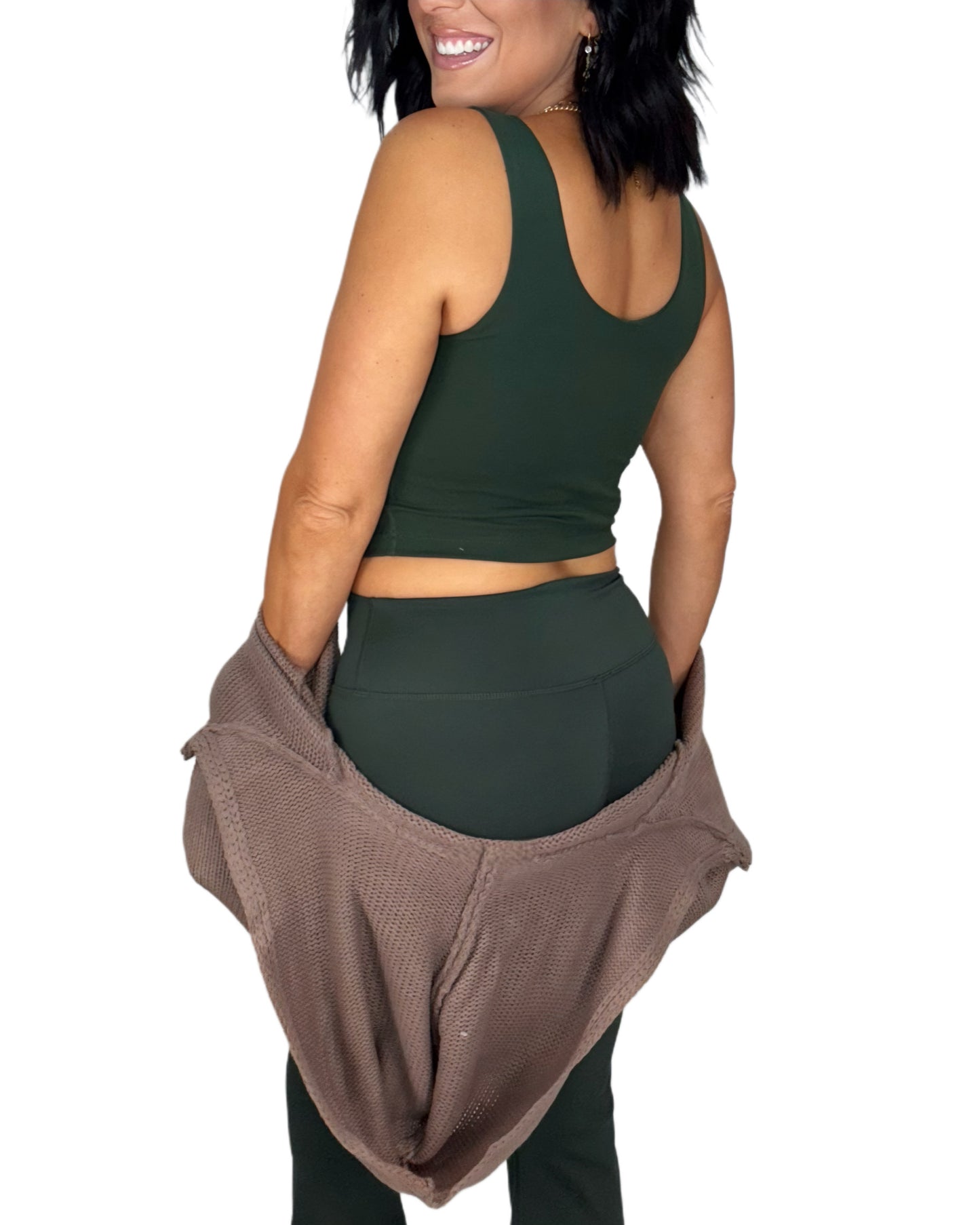 Woman turned around wearing a green athletic outfit with a brown knit jacket on a white background