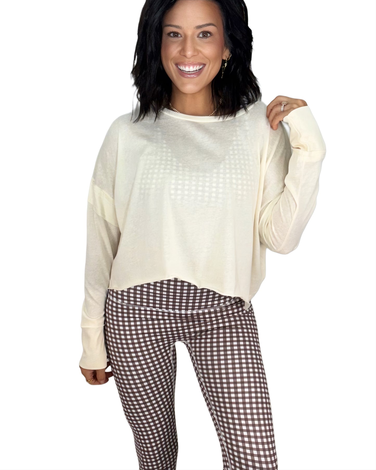 Woman wearing a cream long sleeve top and checkered pants on a white background