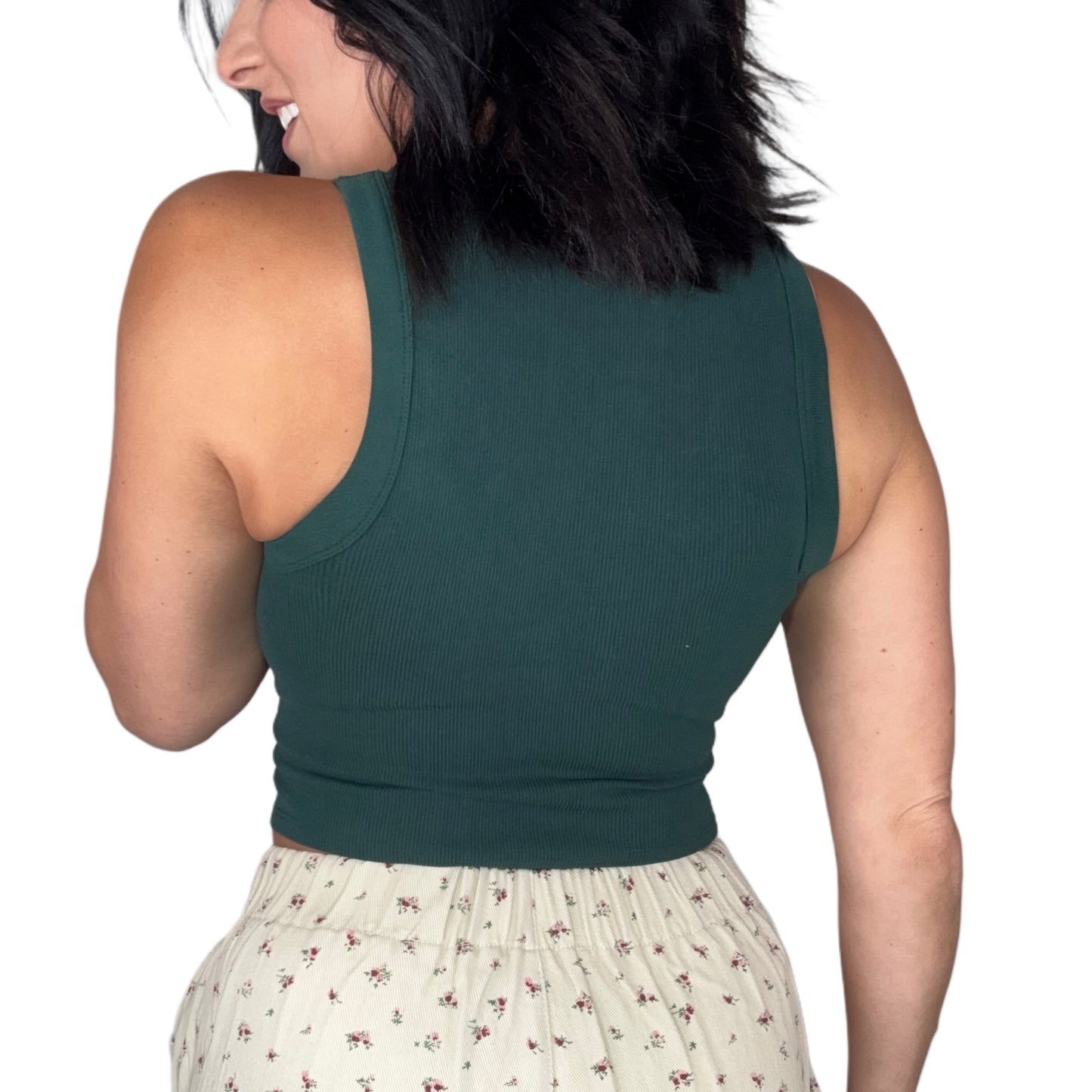 Back profile of a woman wearing a green ribbed sleeveless top and floral shorts on a white background