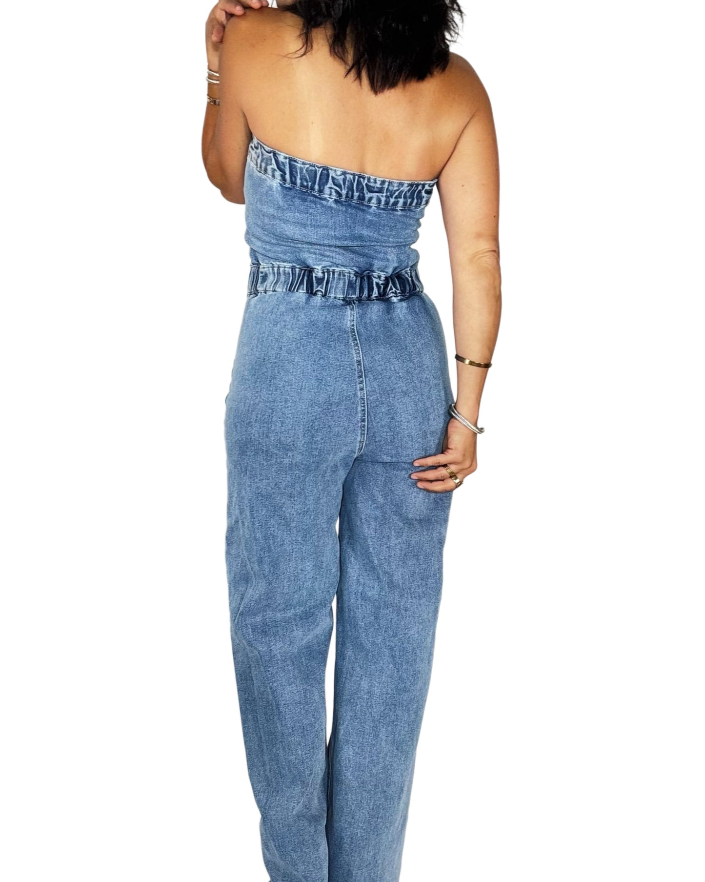 Back profile of a woman wearing a jean jumpsuit on a white background