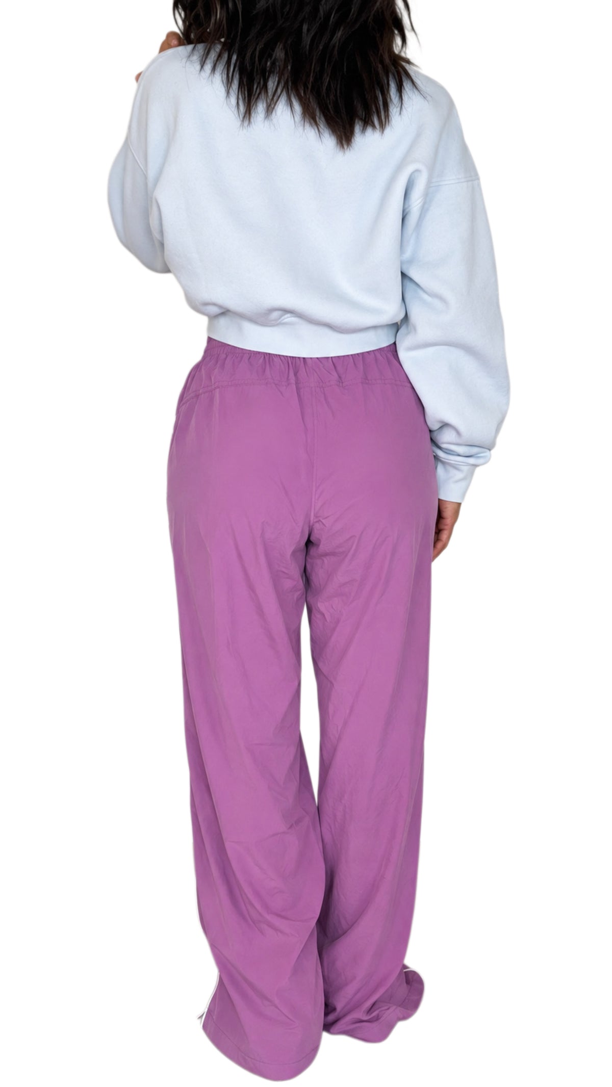 Back profile of a woman wearing mulberry color track pants with a drawstring and white line going down the side with a light blue cropped sweatshirt on a white background