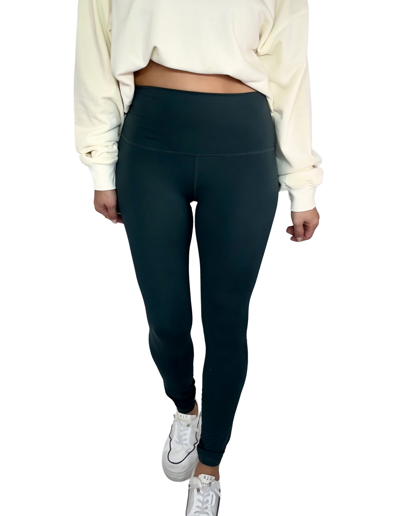 Woman wearing dark green leggings and a cream sweatshirt on a white background