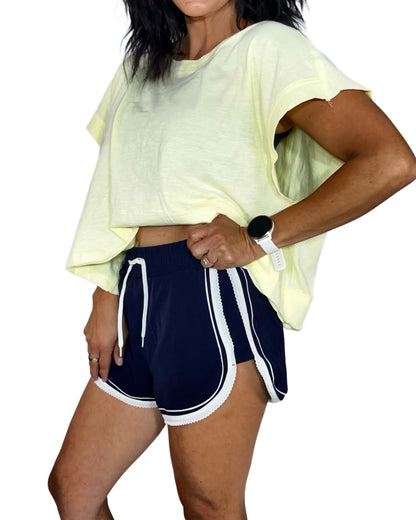 Person wearing a light yellow oversized t-shirt and navy shorts with white stripes on a white background