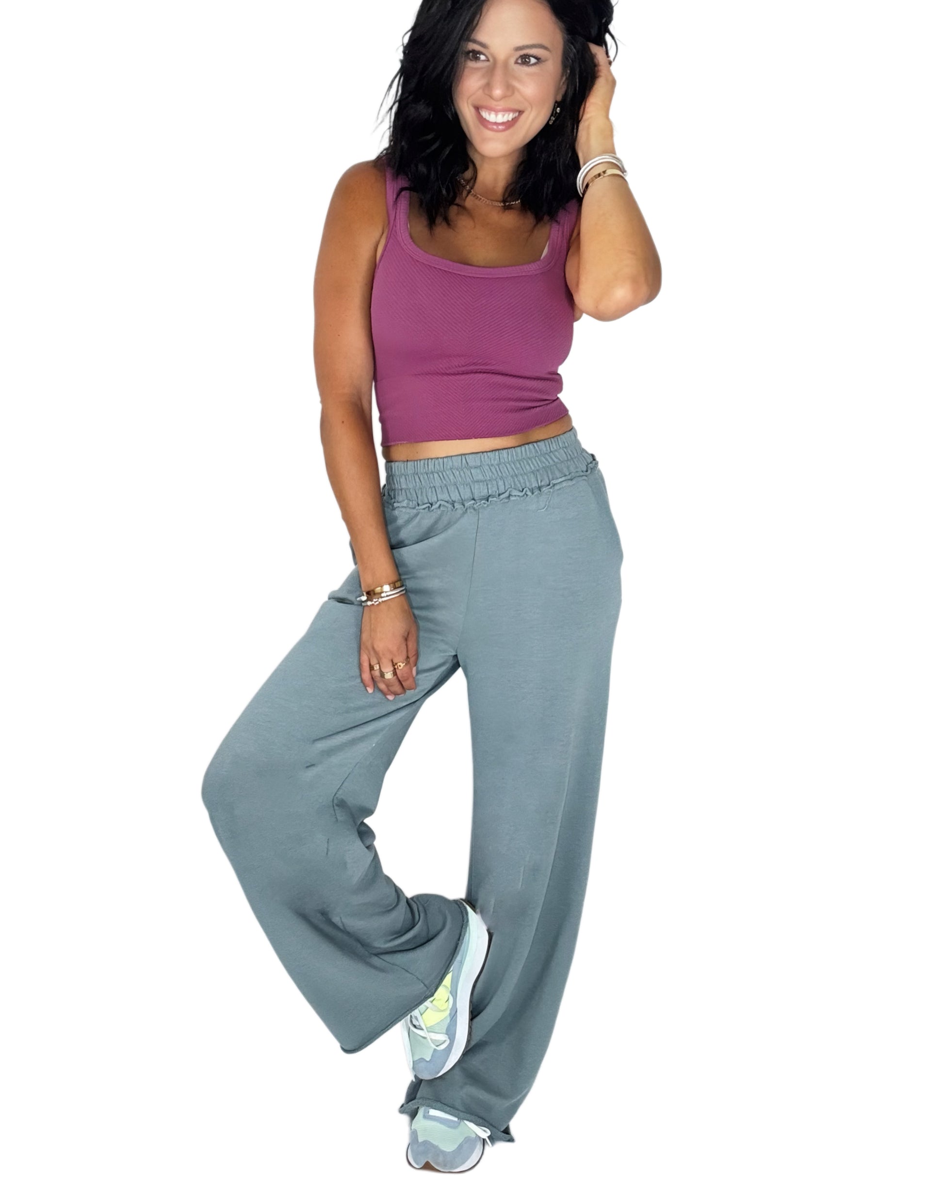 Woman wearing a ribbed mauve tank with grey blue sweat pants on a white background
